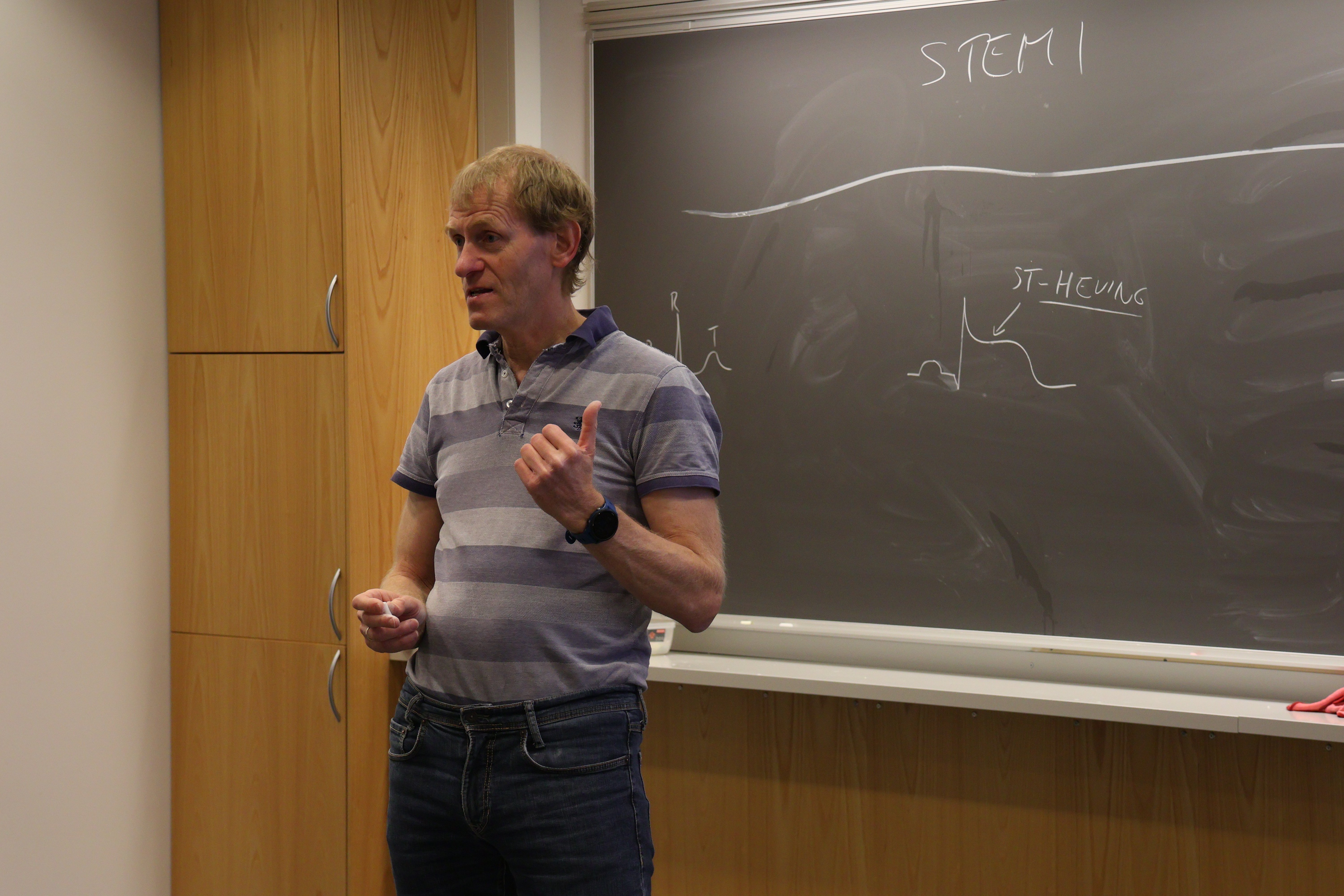 Mann som står foran en tavle og ser utover klasserommet i en læringssituasjon.