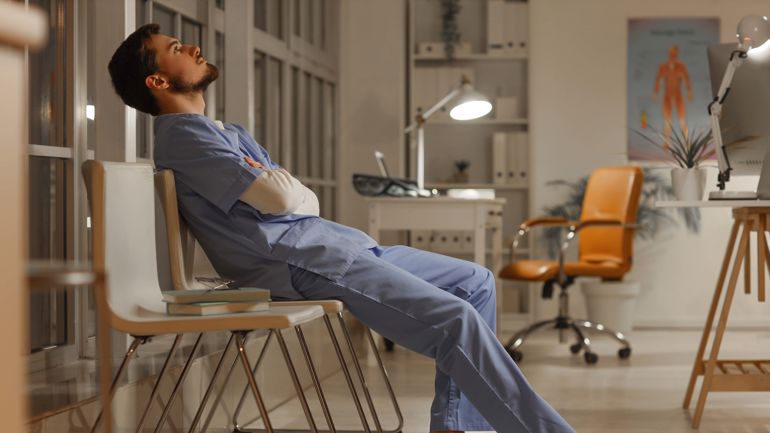 Mannlig sykepleier i uniform ligger bakover på en stol og ser opp i taket.