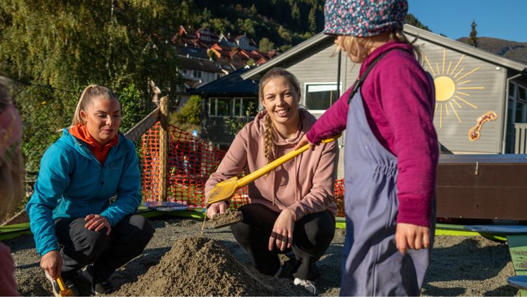 To voksne og et barn som leker i en sandkasse