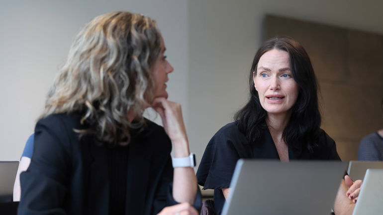 To kvinner sitter foran et bord. De ser på hverandre.