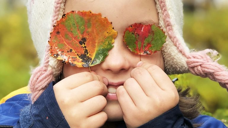Bilete av eit barn som held lauv foran begge augene.