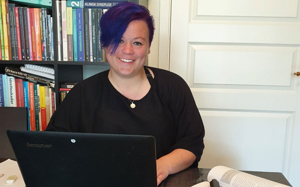 Kvinne sit framfor ein laptop og smiler.