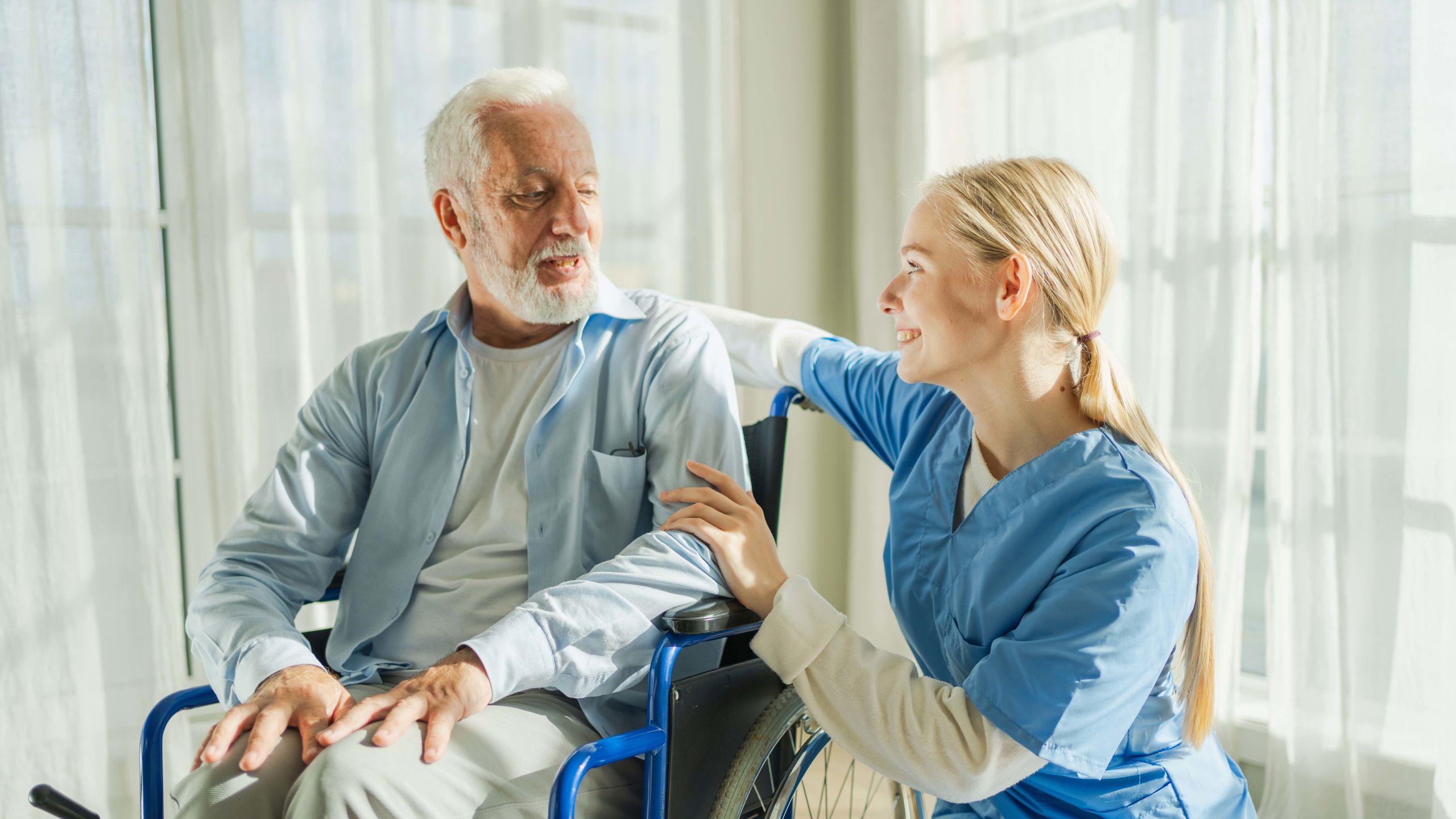 Kvinnelig sykepleier hjelper eldre mann i rullestol.