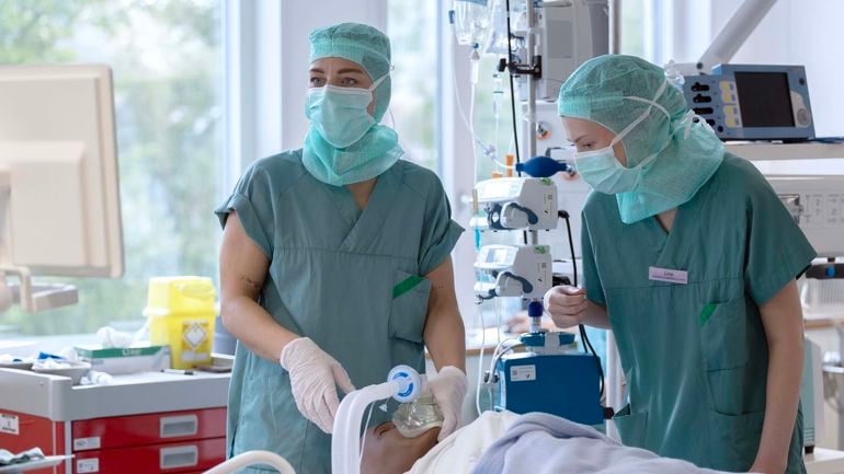 To sykepleiere står over pasient med en maske.