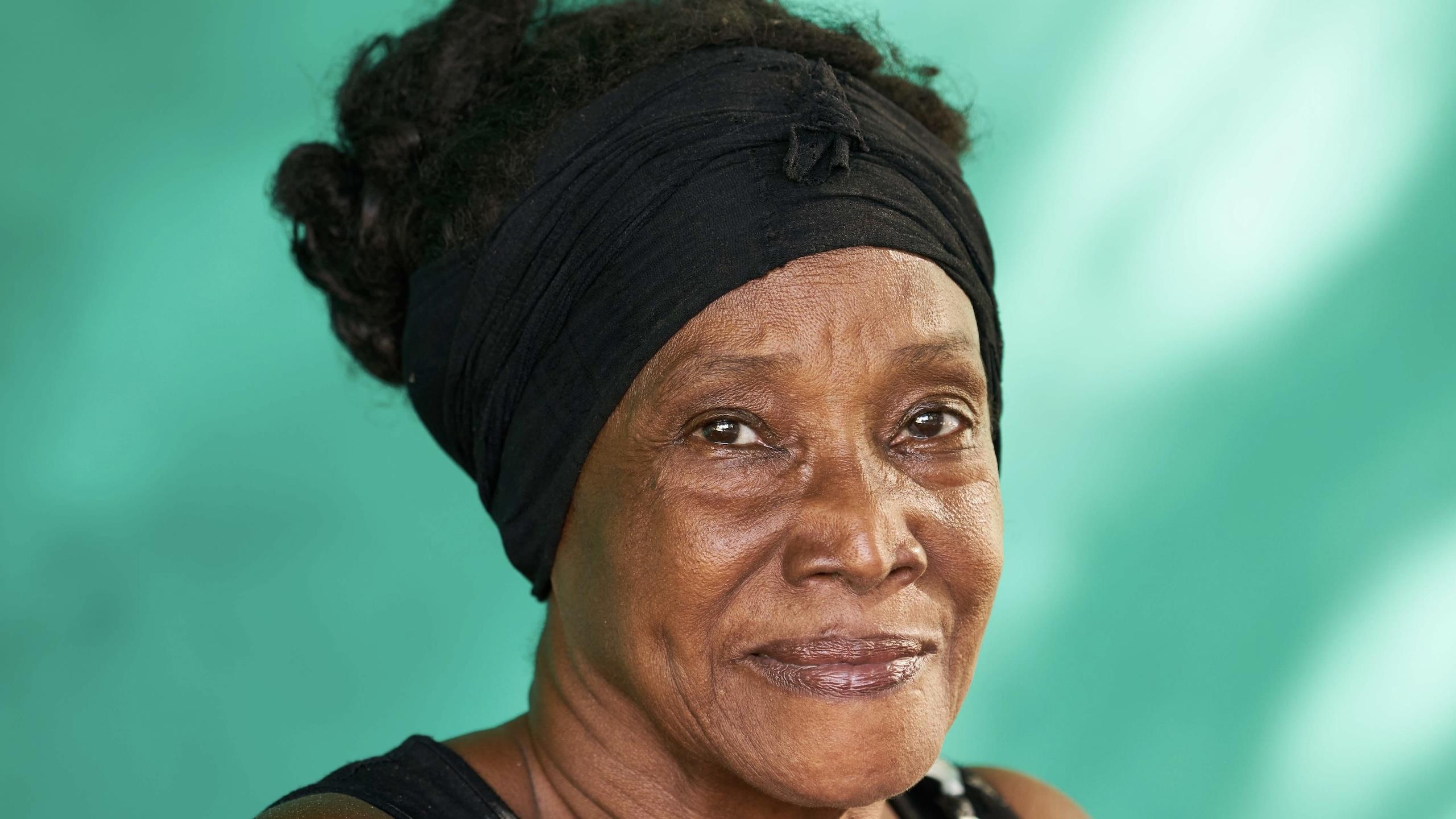 Eldre cubansk kvinne ser inn i kamera. Grønn bakgrunn.