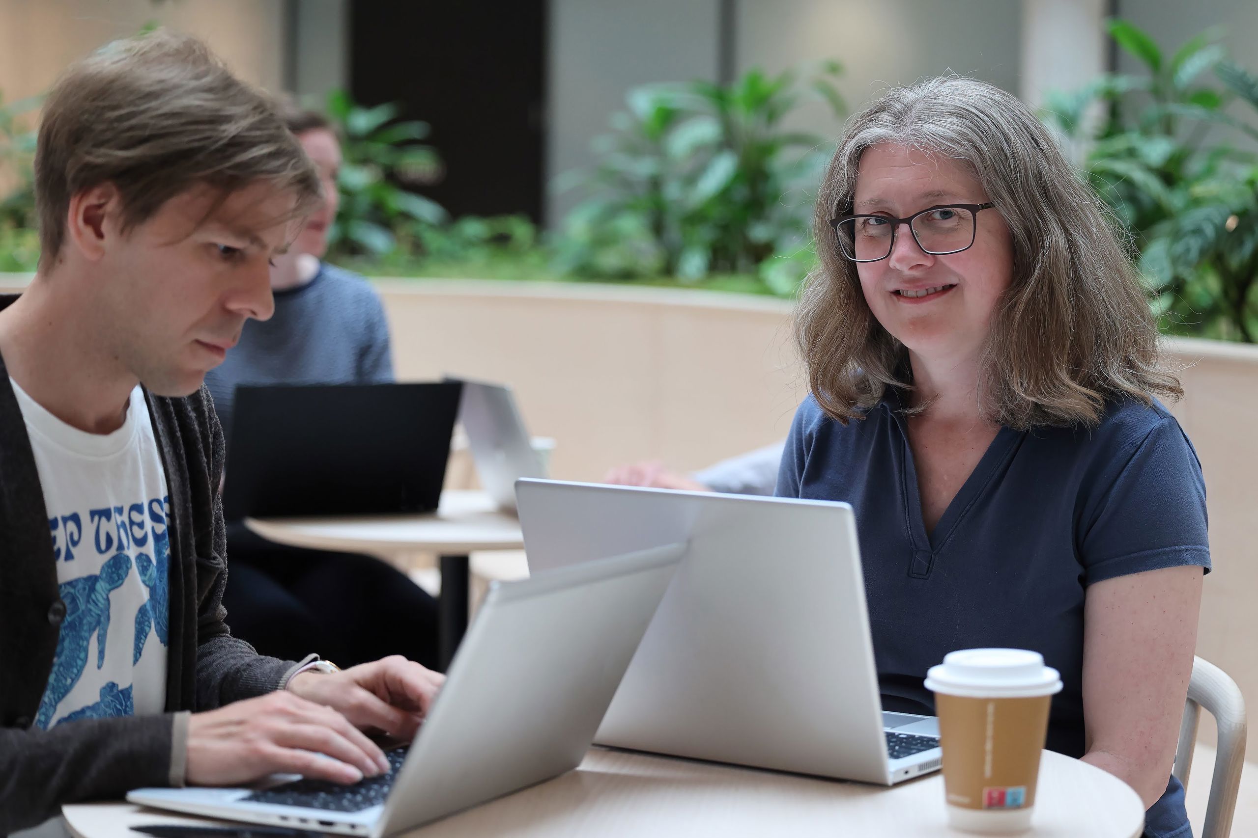 En kvinne og en mann sitter med hver sin pc rundt et bord.