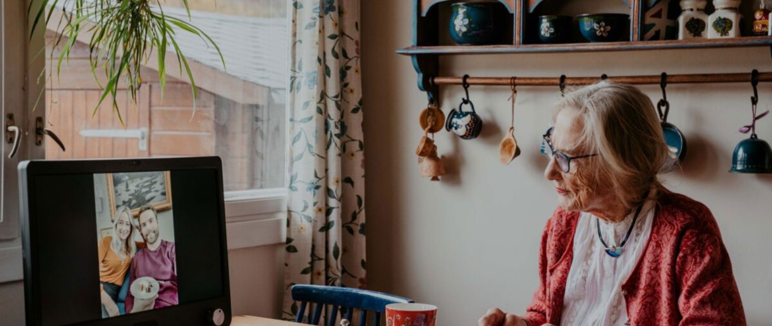 En eldre person sitter og spiser mens datamaskinen er koblet til en videosamtale med to personer.