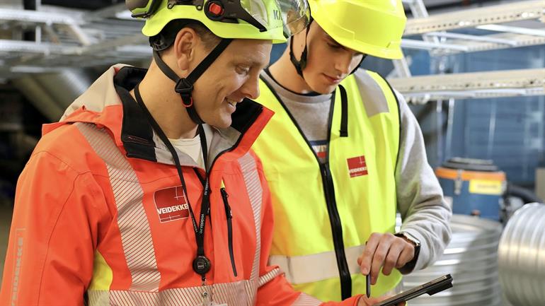 To arbeidstakere på en byggeplass snakker sammen.