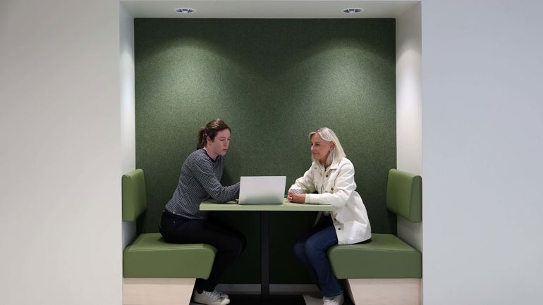 To personer sitter ovenfor hverandre ved et arbeidsbord og diskuterer.