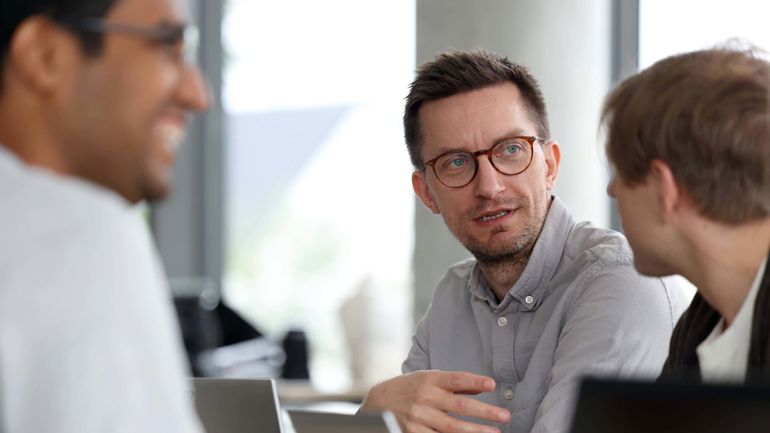 Mann med briller sitter sammen med to andre personer.