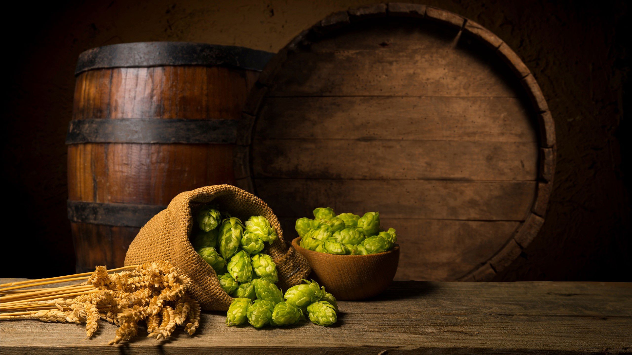 Humle og malt på et bord, og to tønner i bakgrunnen.