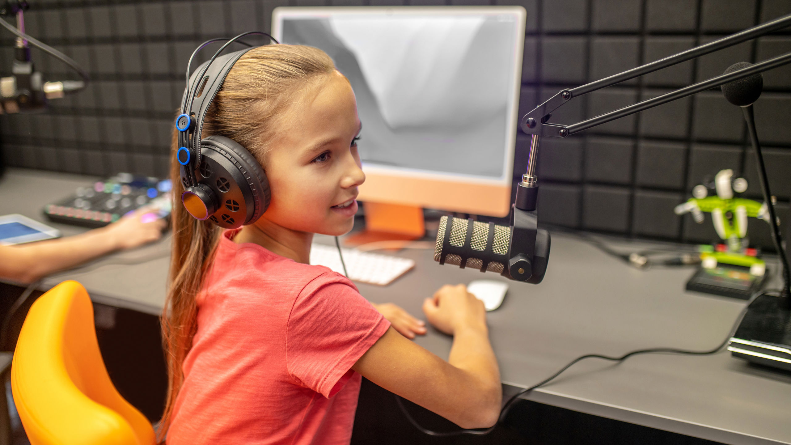 Jente i rød t-skjorte sitter med hodetelefoner på ørene og prater inn i en mikrofon som er knyttet til en pc.