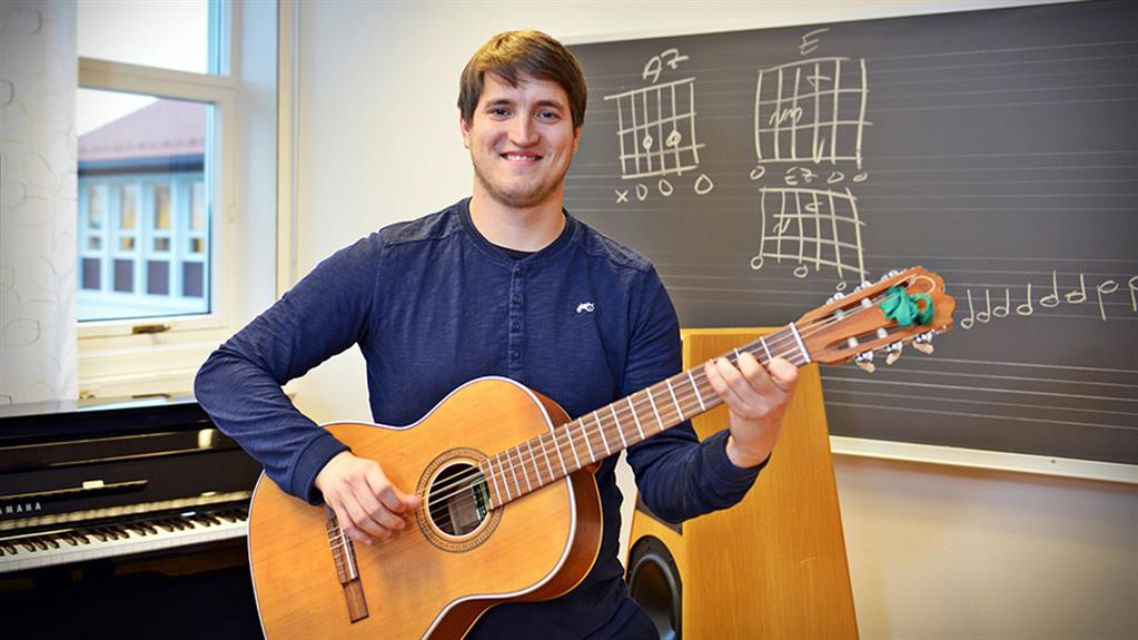 Mannleg student med gitar foran tavle med notar. 