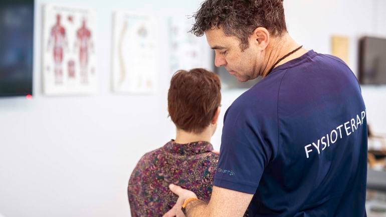 Ein fysioterapeut som kjenner på ryggen til ein pasient.