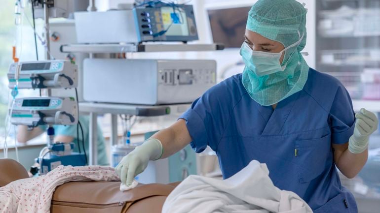 Sykepleier i uniform tørker av magen på en dukke med bomull.