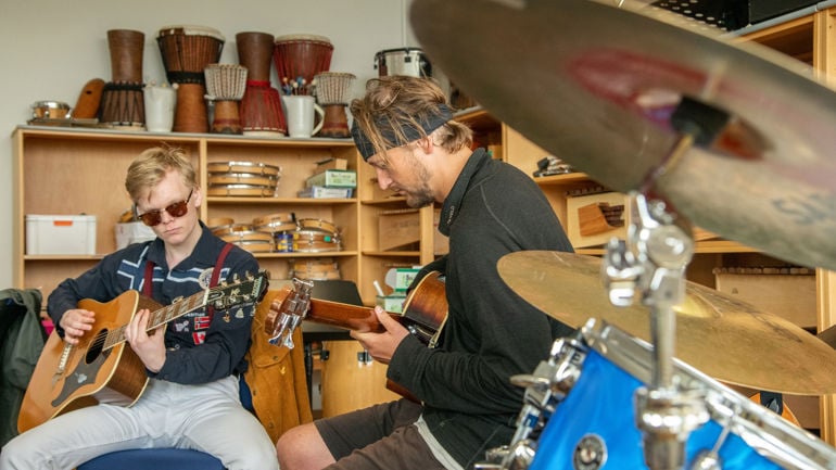 To person som sitter rundt andre instrumenter og spiller gitar