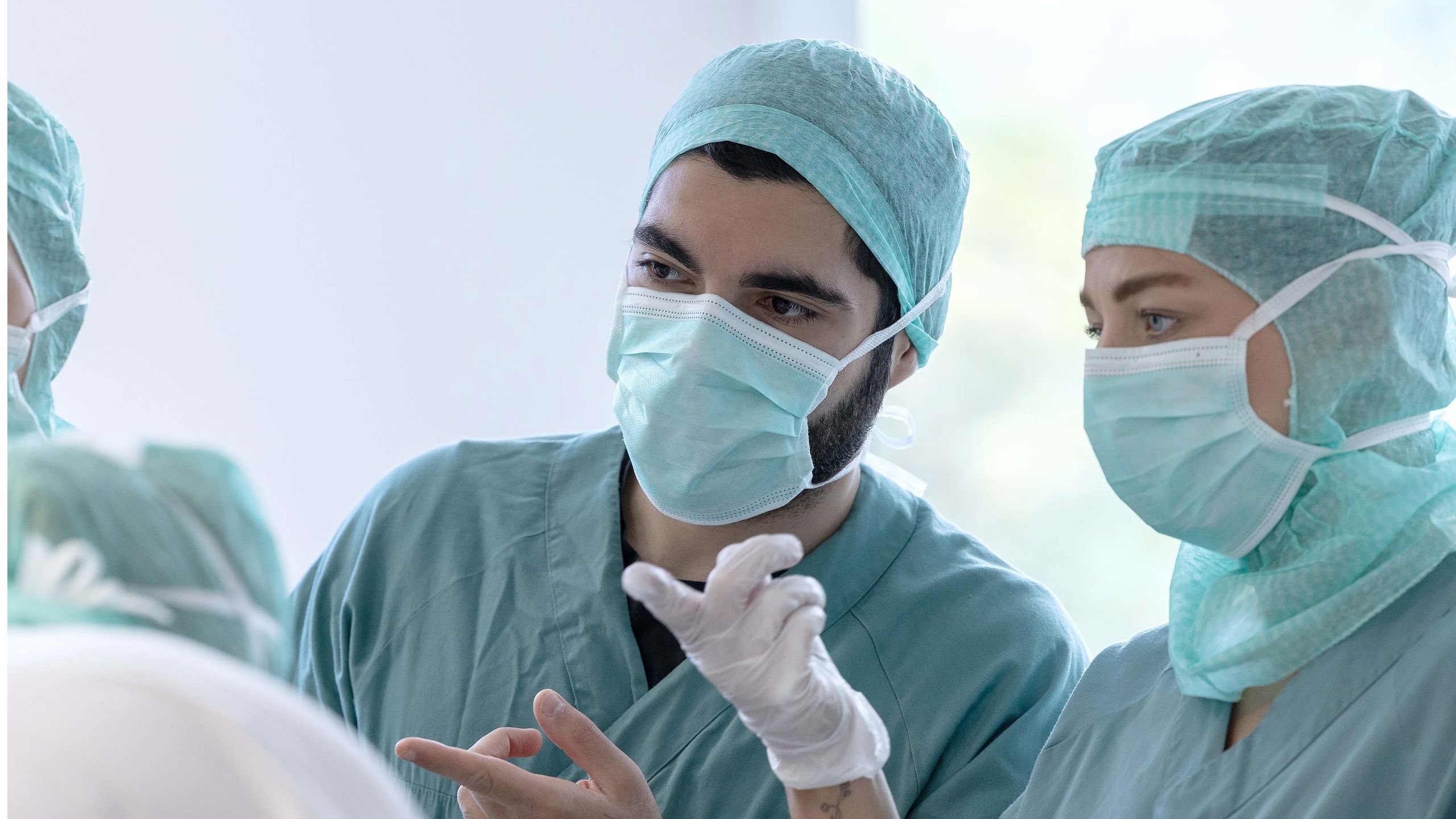 To sykepleiere med uniform, hårnett og munnbind ser på noe og peker.