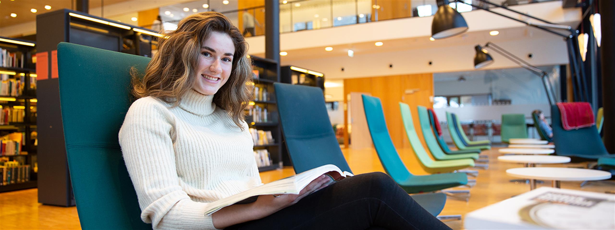 A student sitting in a chair at the library with a book.