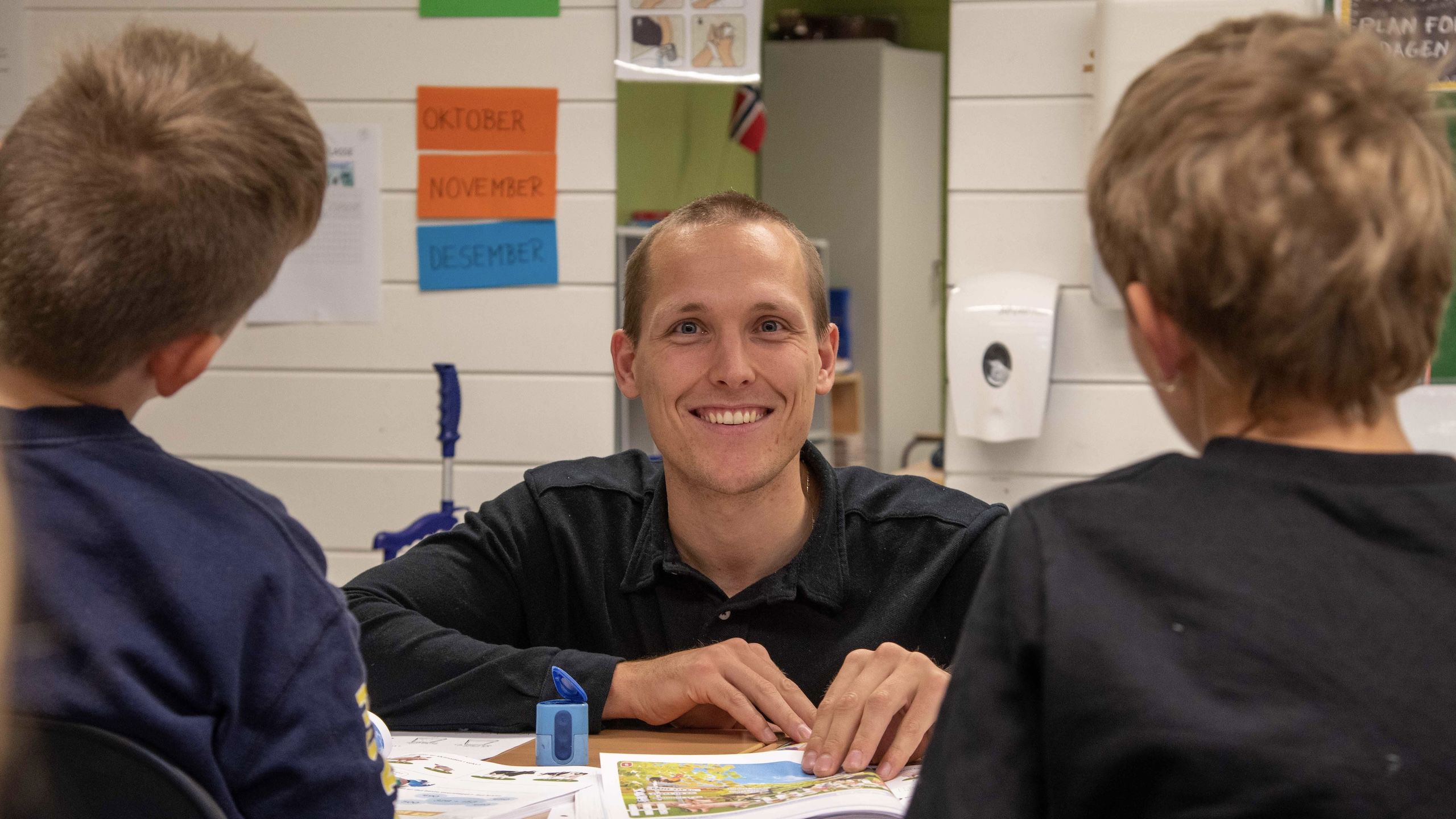 En smilende ung mann som ser i kamera og hjemler to barn.