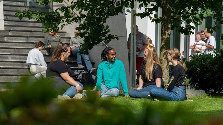 Studentar sit på plenen på campus.