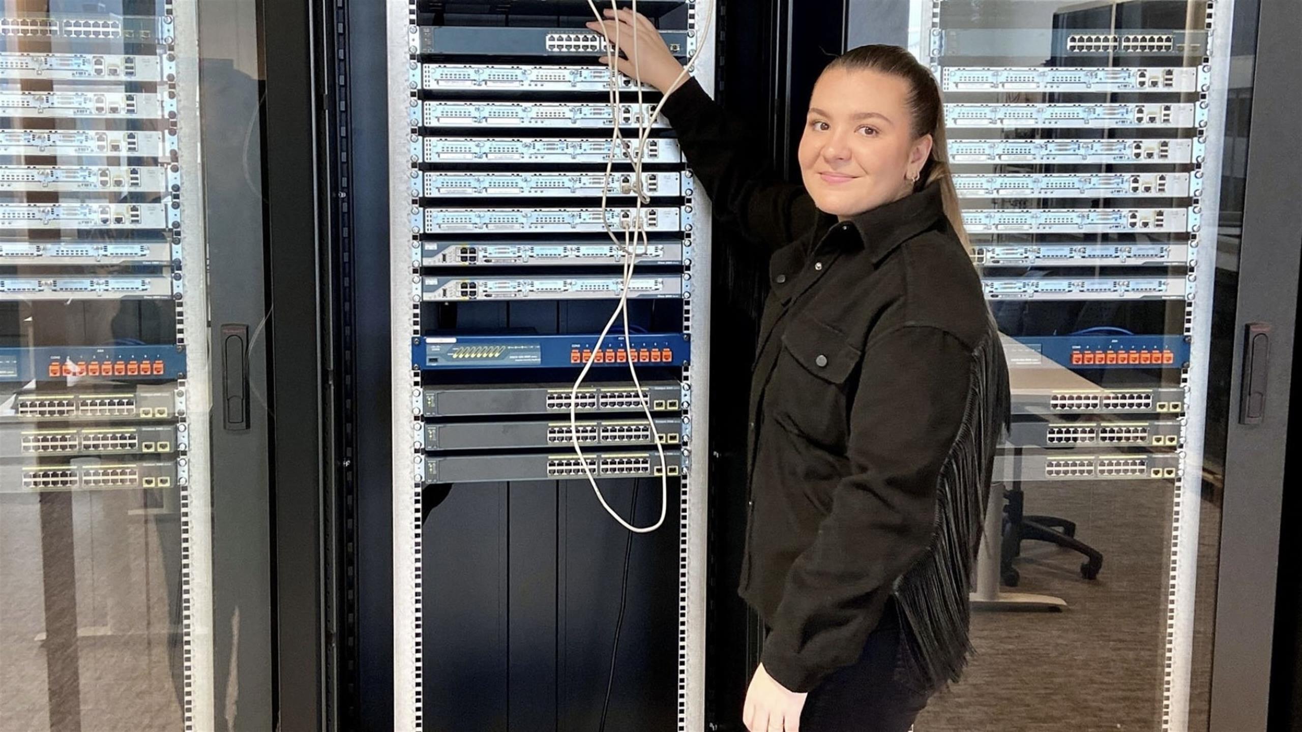 A smiling woman in front of a cabinet of servers.