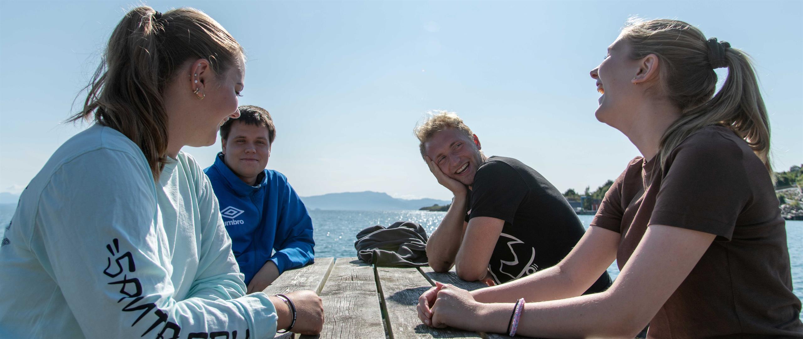 Four young people at a table by the sea.