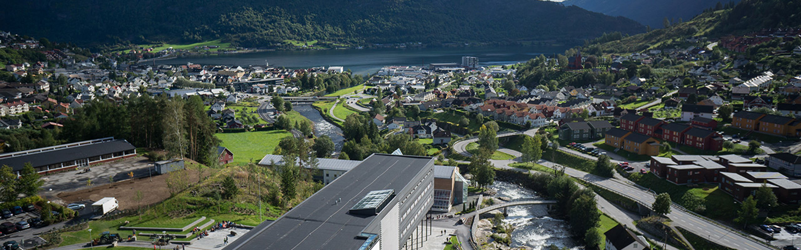 Dronebilde over campus og Sogndal, med bygningar, fjell og fjord.