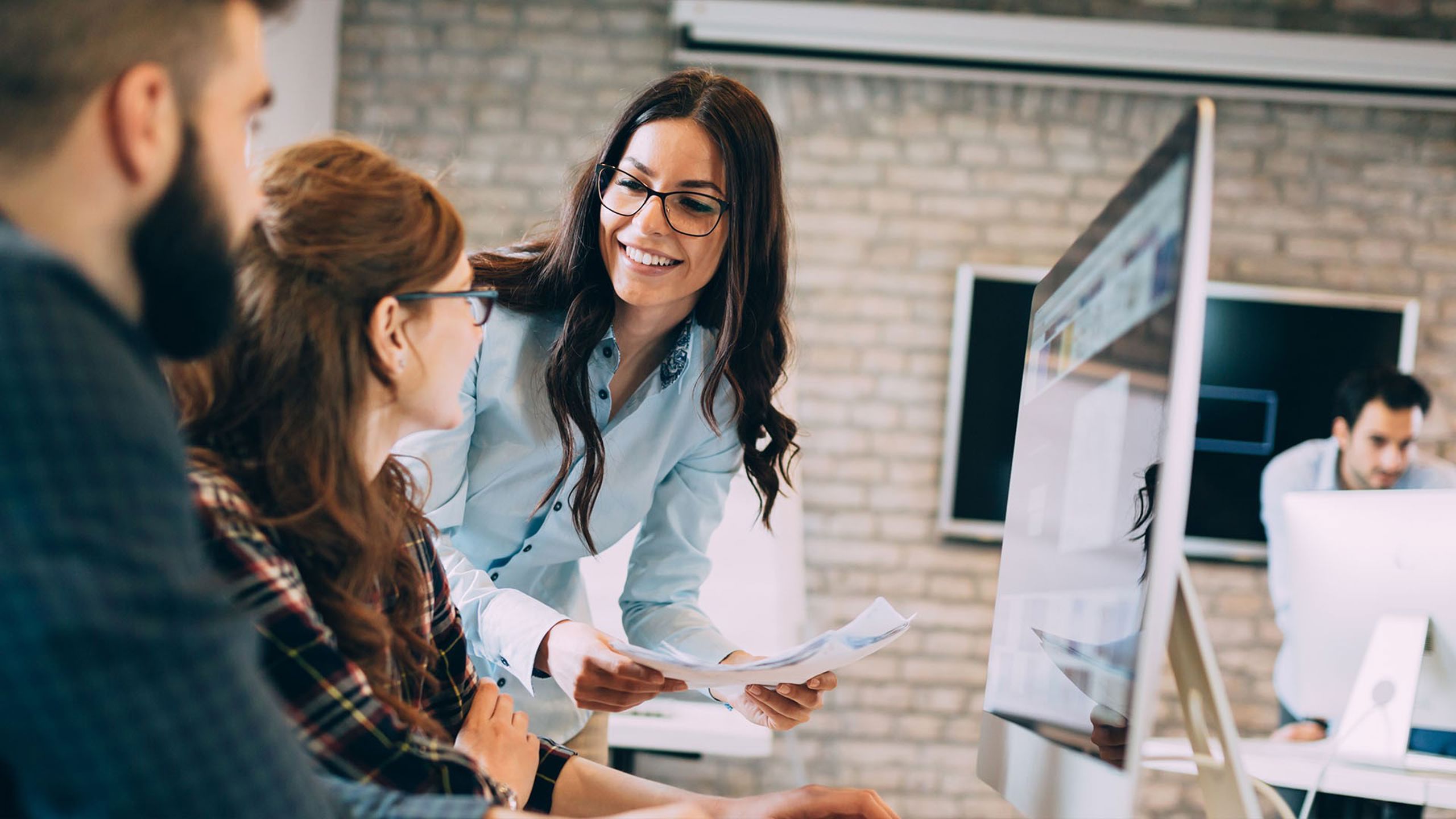 To kvinner som jobber på pc og går gjennom papirer på arbeidsplass
