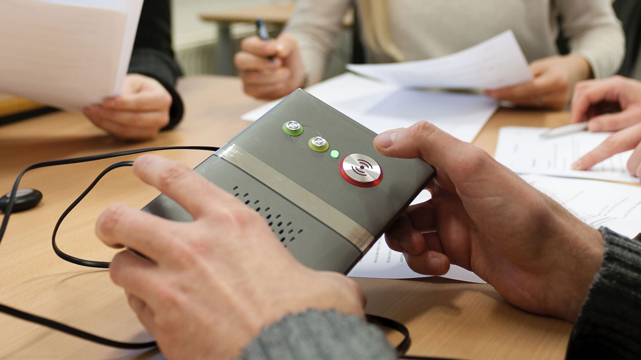 Utsnitt av flere hender som arbeider med diverse papir og teknologi.